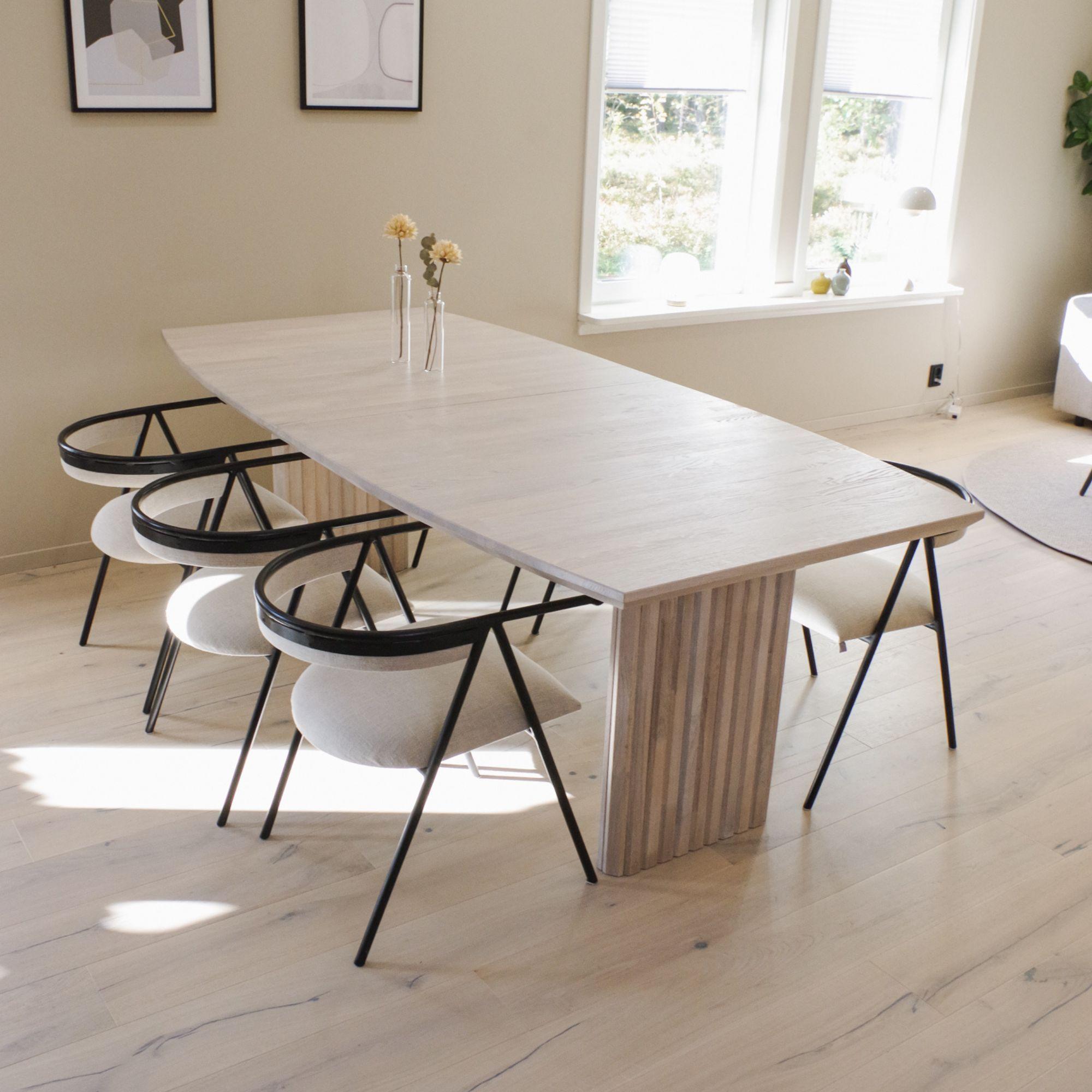 Ett ljust matbord med ribbade ben, placerad i ett ljust vardagsrum.