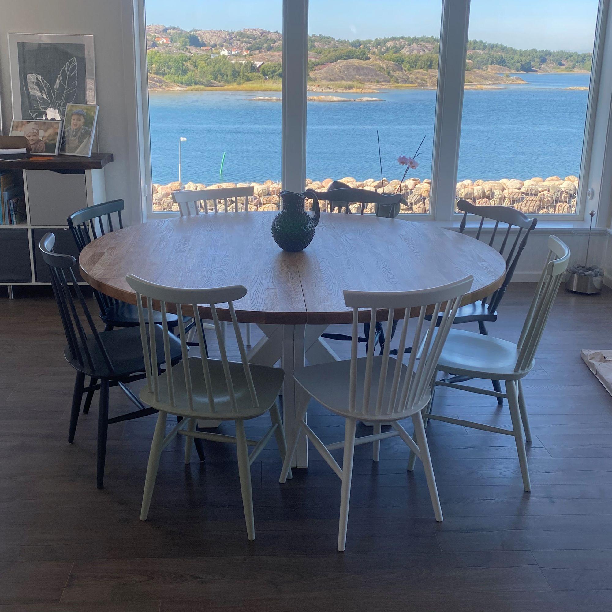 Runt matbord med ljusa stolar placerad i ett vardagsrum med havsutsikt